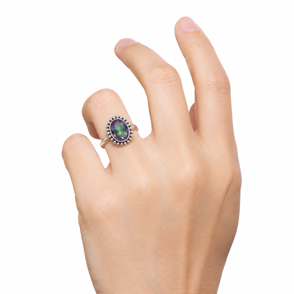 A hand wearing a silver ring with an oval iridescent green and blue stone, set against a plain white background.